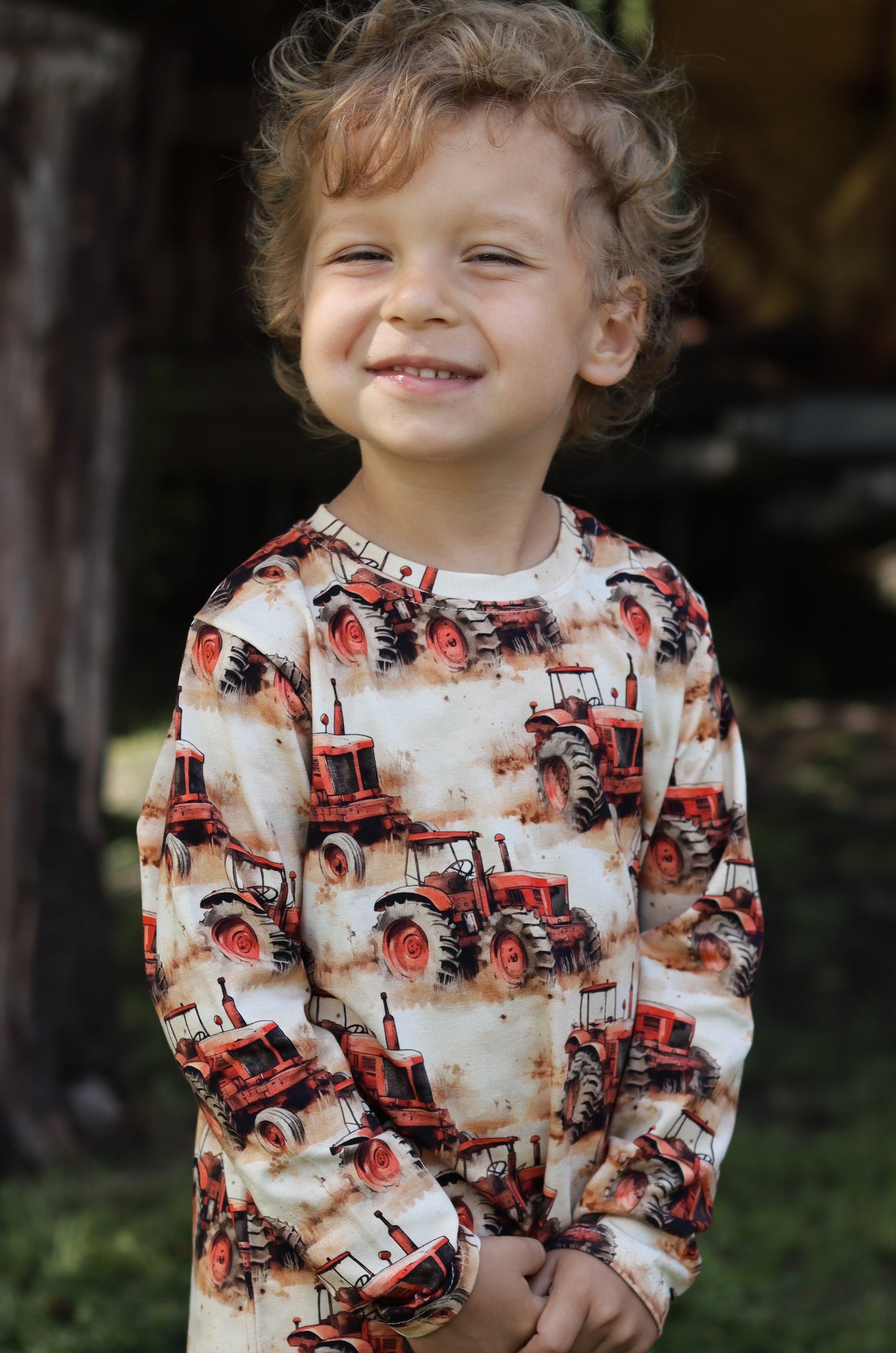 Child wearing a patterned shirt standing outdoors with trees and grass in the background