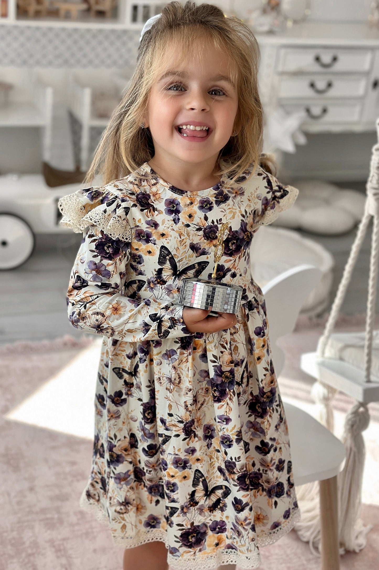 Young girl in a floral dress standing in a room with a white dresser and toy car.