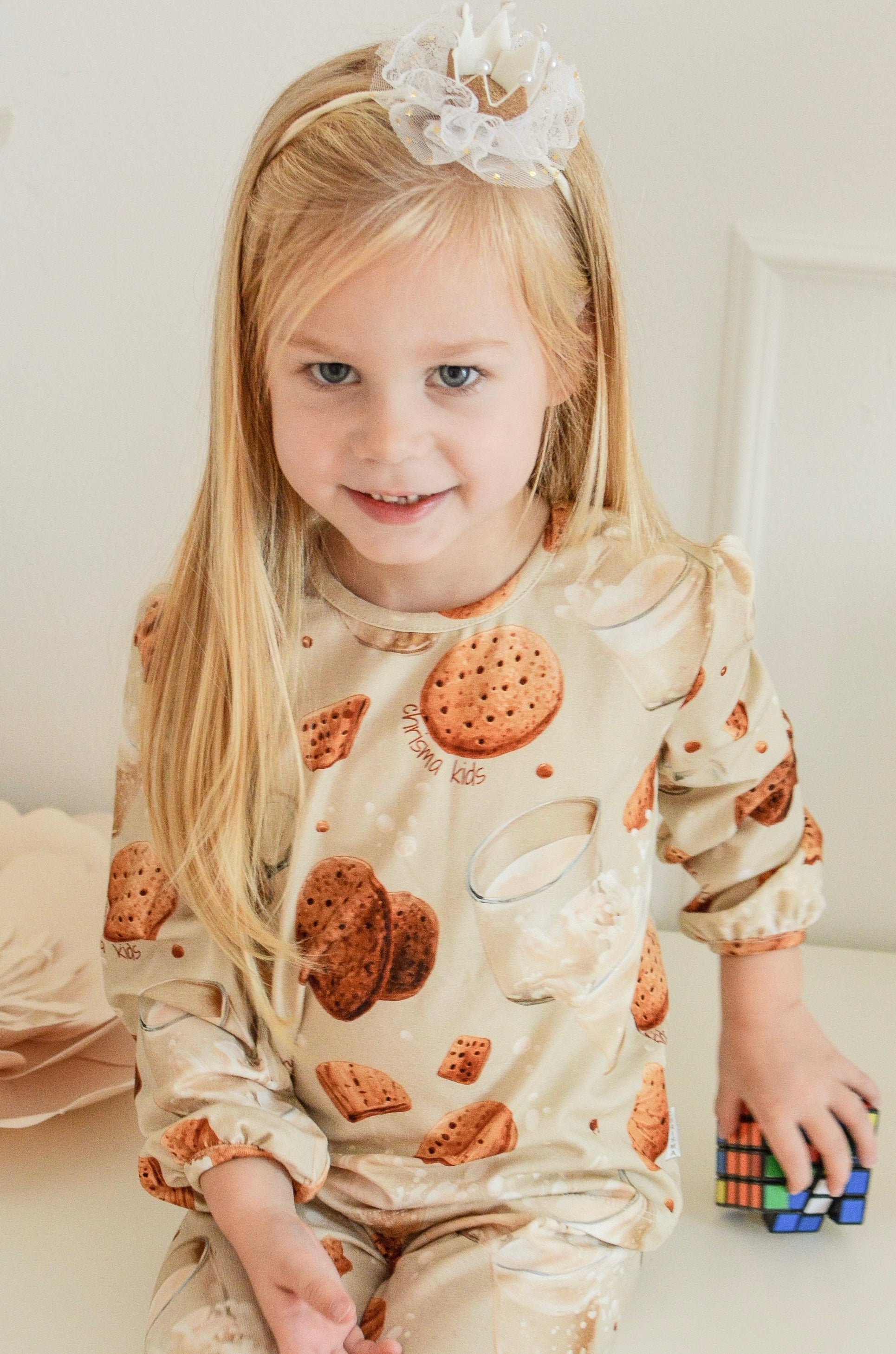 Child wearing pajamas with cookie pattern sitting on a couch.