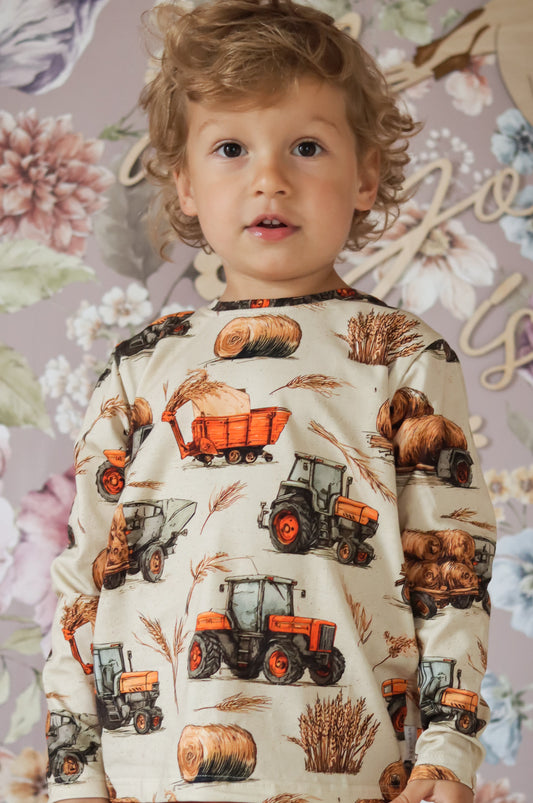 Child wearing a sweater with tractor print against a floral wall.