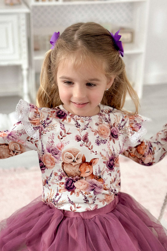 Young girl in a floral top and pink tutu skirt on a swing.