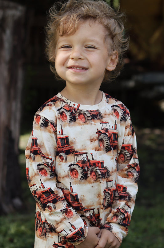 Child wearing a patterned shirt standing outdoors with trees and grass in the background