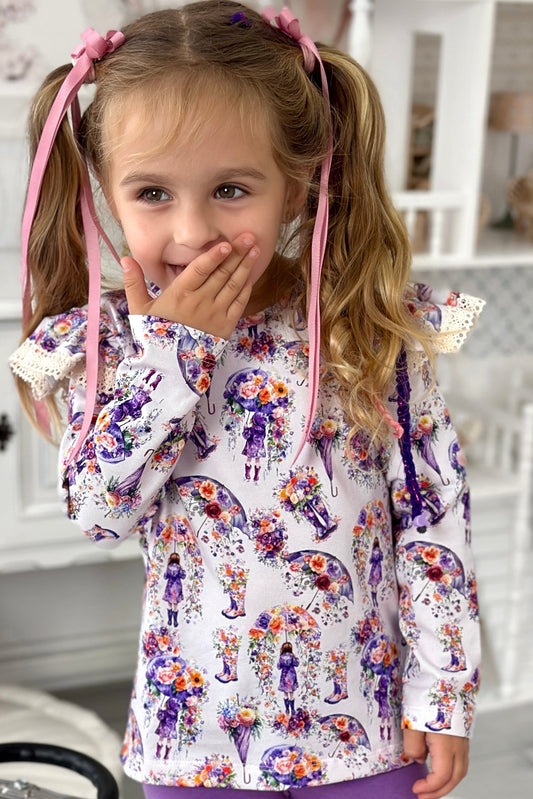 Young girl in a floral shirt and purple leggings standing next to a toy car in a playroom.