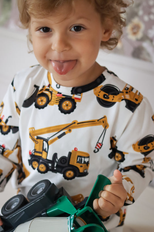 Child wearing a onesie with construction vehicle patterns, holding a toy truck.