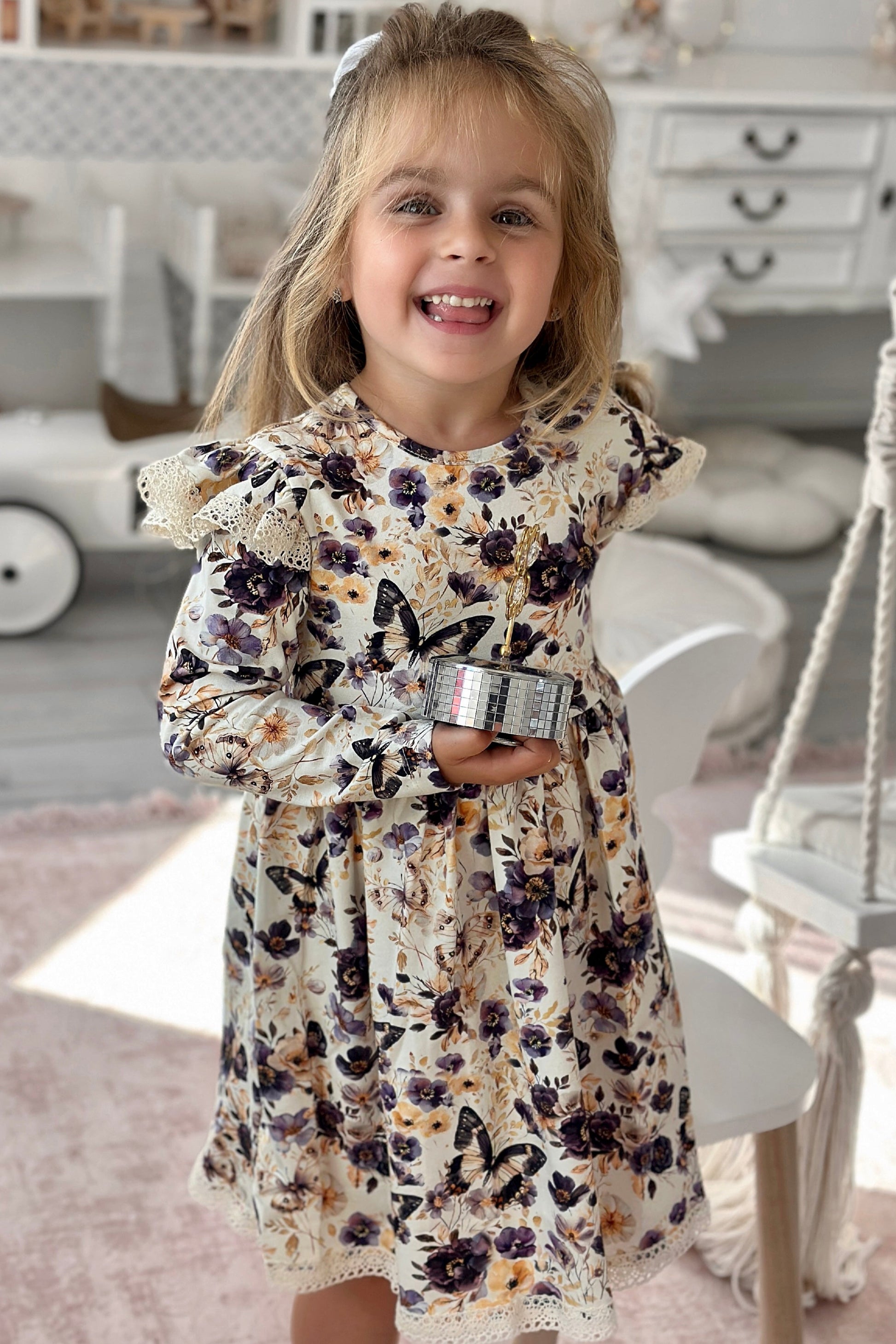 Young girl in a floral dress standing in a room with a white dresser and toy car.
