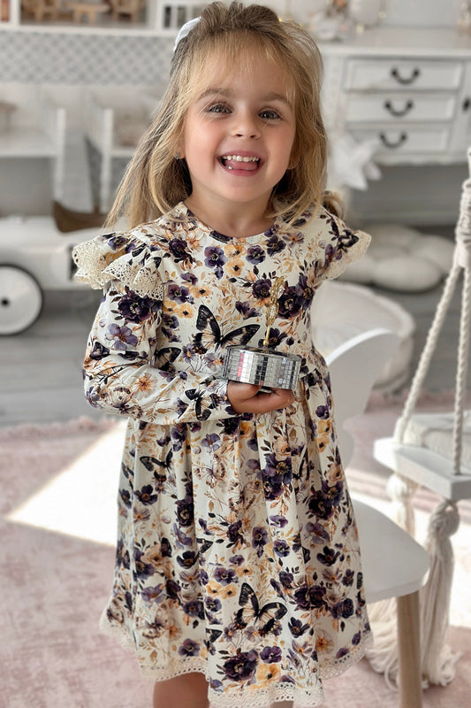 Young girl in a floral dress standing in a room with a white dresser and toy car.
