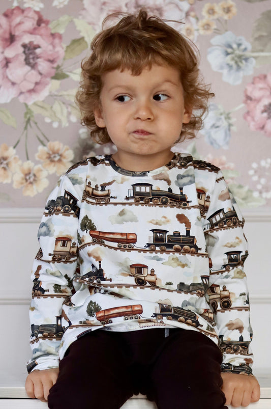 Child wearing a sweater with train pattern against a floral wallpaper background