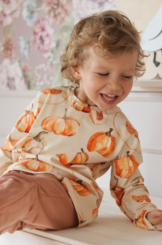 Child wearing a pumpkin-patterned shirt in a room with floral decorations
