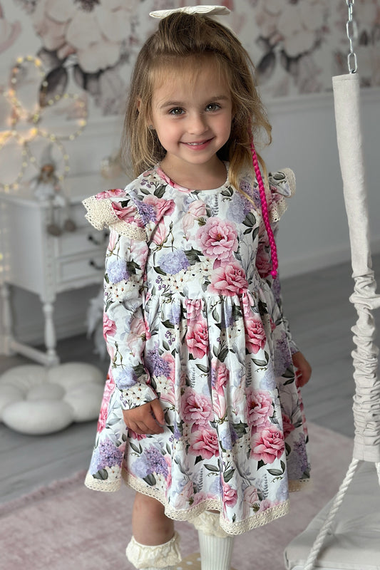 Young girl in a floral dress standing in a decorated room with a swing and fairy lights.