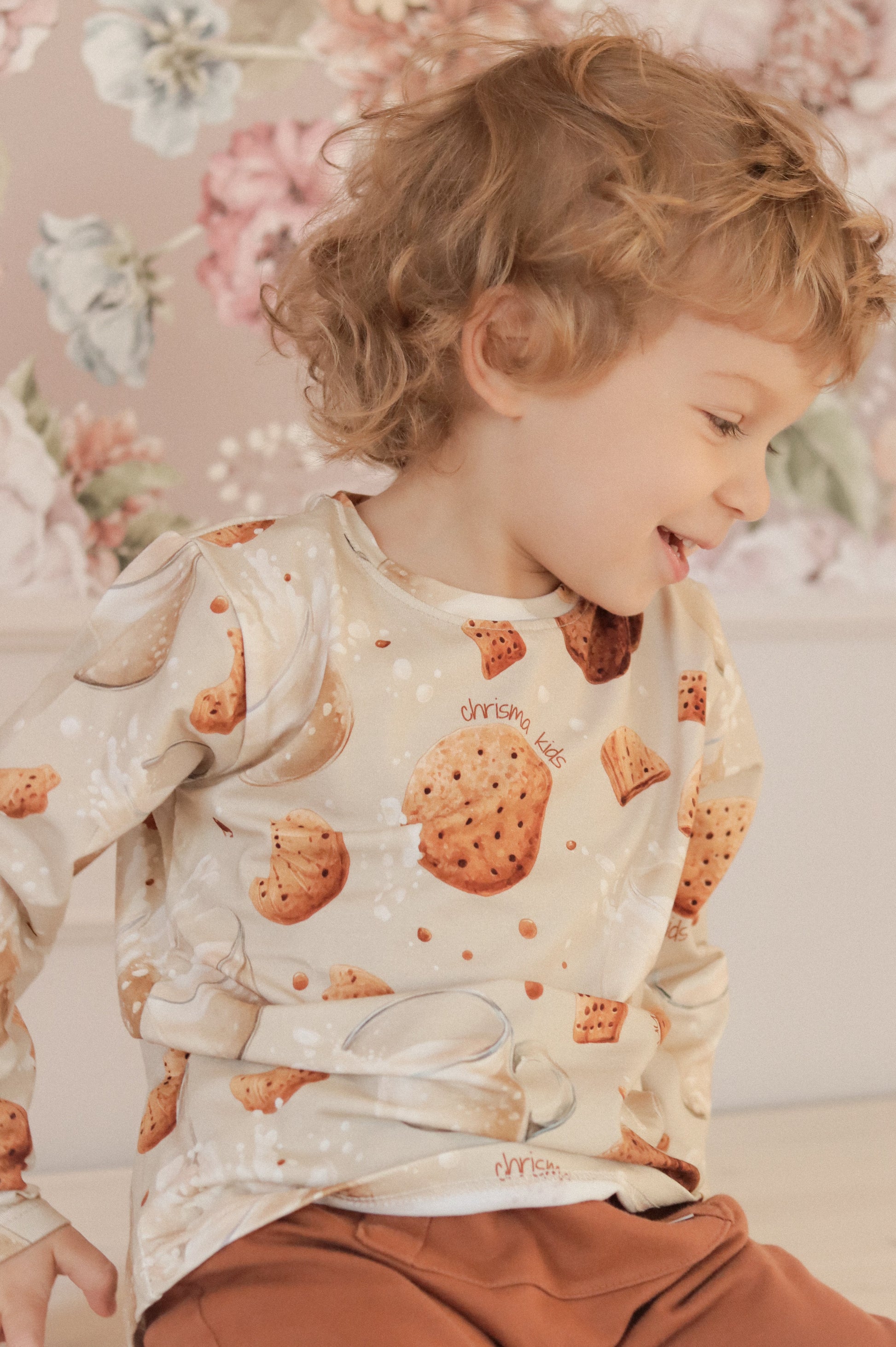 Child wearing a patterned shirt with cookies in a room with floral wallpaper